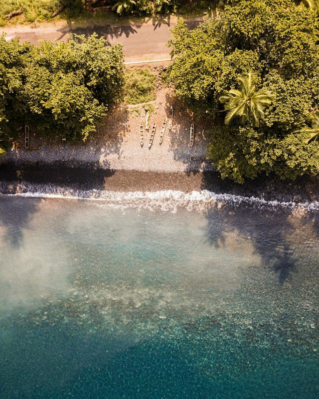 Una vista aerea dall'alto di canoe su una spiaggia di ciottoli, dove l'acqua cristallina turchese incontra una costa lussureggiante e alberata.