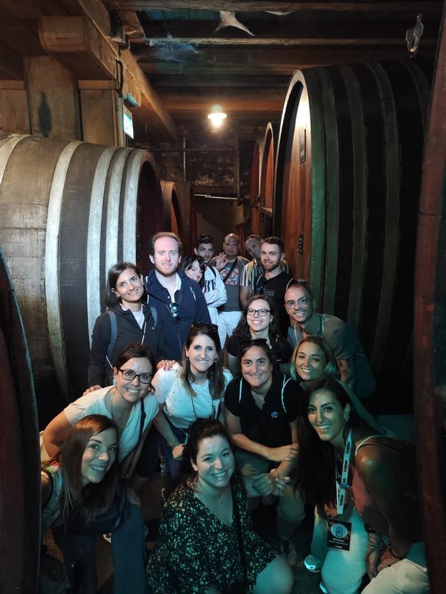 Un gruppo WeRoad in viaggio posa per una foto in una cantina tra grandi botti di legno.