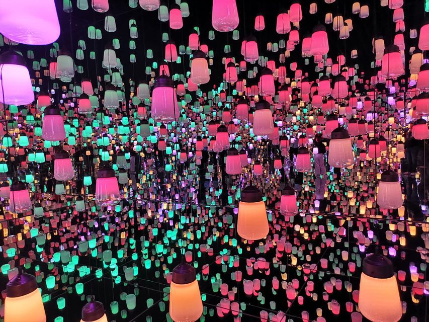 An art installation of numerous colorful hanging lanterns reflected infinitely in a dark, mirrored room.