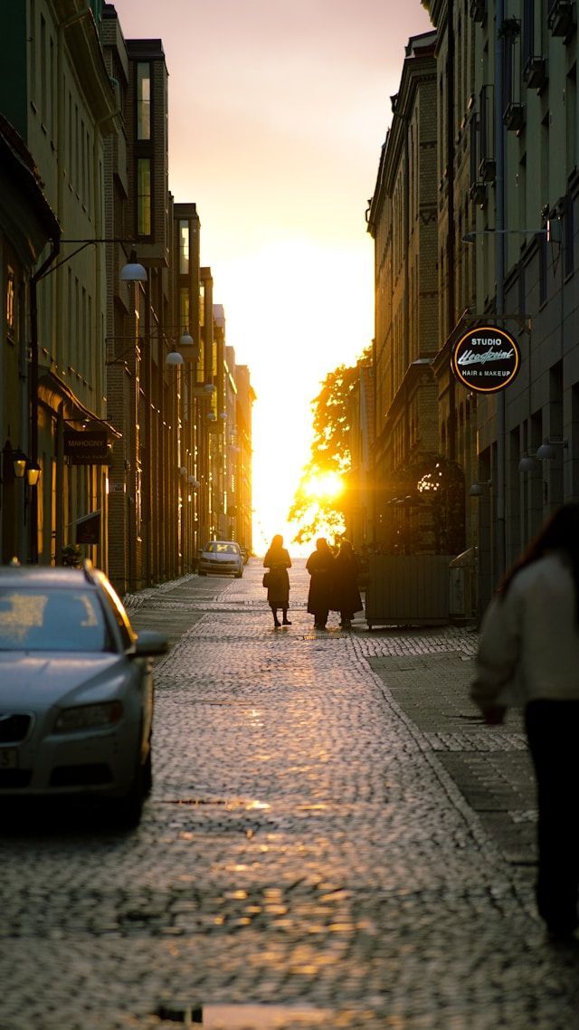 Menschen zeichnen sich vor einem goldenen Sonnenuntergang am Ende einer engen, kopfsteingepflasterten Stadtgasse ab.