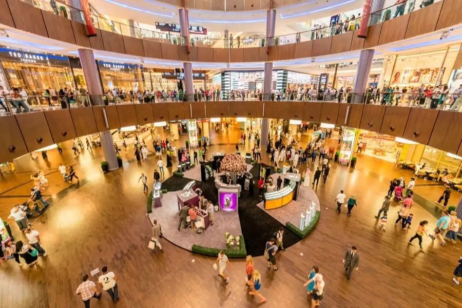 An overhead view of a busy, multi-level shopping mall with a circular atrium and many people walking on the wooden floors.