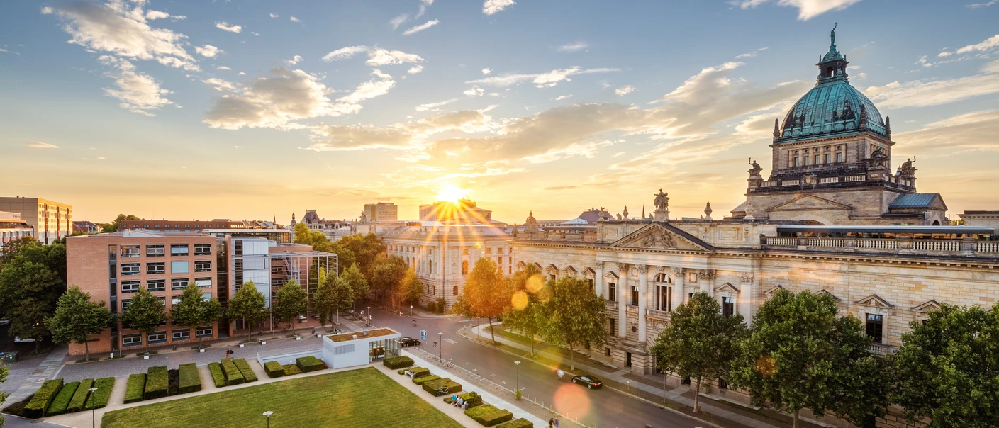 Luftaufnahme einer Stadtlandschaft mit historischem Gebäude und großer Kuppel, gebadet im goldenen Licht der untergehenden Sonne.