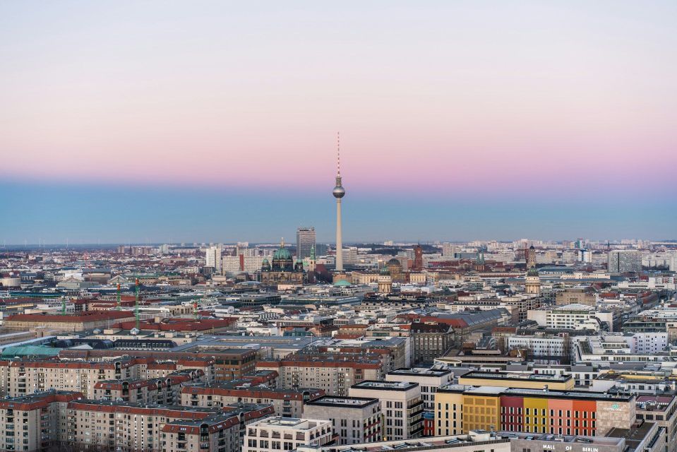 Luftaufnahme der Berliner Skyline mit dem Fernsehturm im Mittelpunkt unter einem rosa-blauen Verlaufs-Himmel bei Sonnenuntergang.