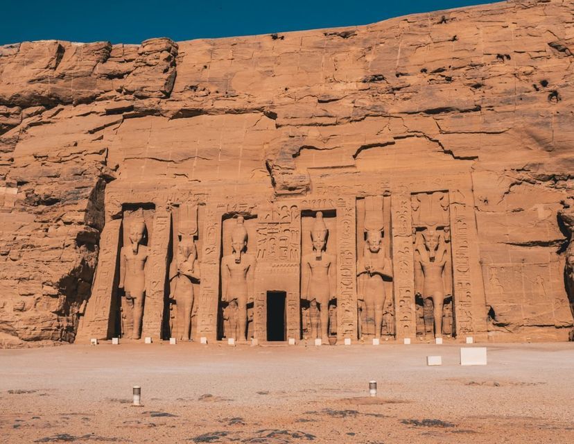 La facciata di un grande tempio scolpito in una scogliera di arenaria, con statue colossali e geroglifici ai lati di un ingresso centrale.