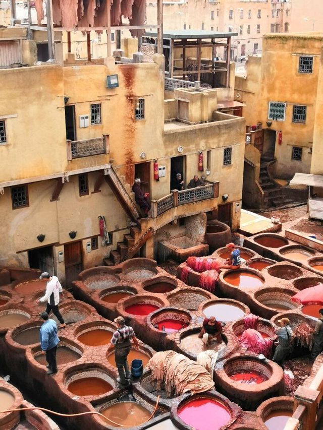 Men working at a traditional outdoor tannery surrounded by large, circular stone vats filled with colorful dyes.