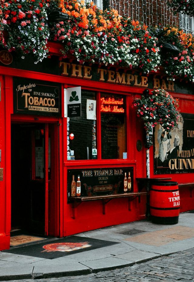 Die leuchtend rote Fassade des The Temple Bar Pub in Dublin, geschmückt mit bunten Blumenkästen über dem Eingang.