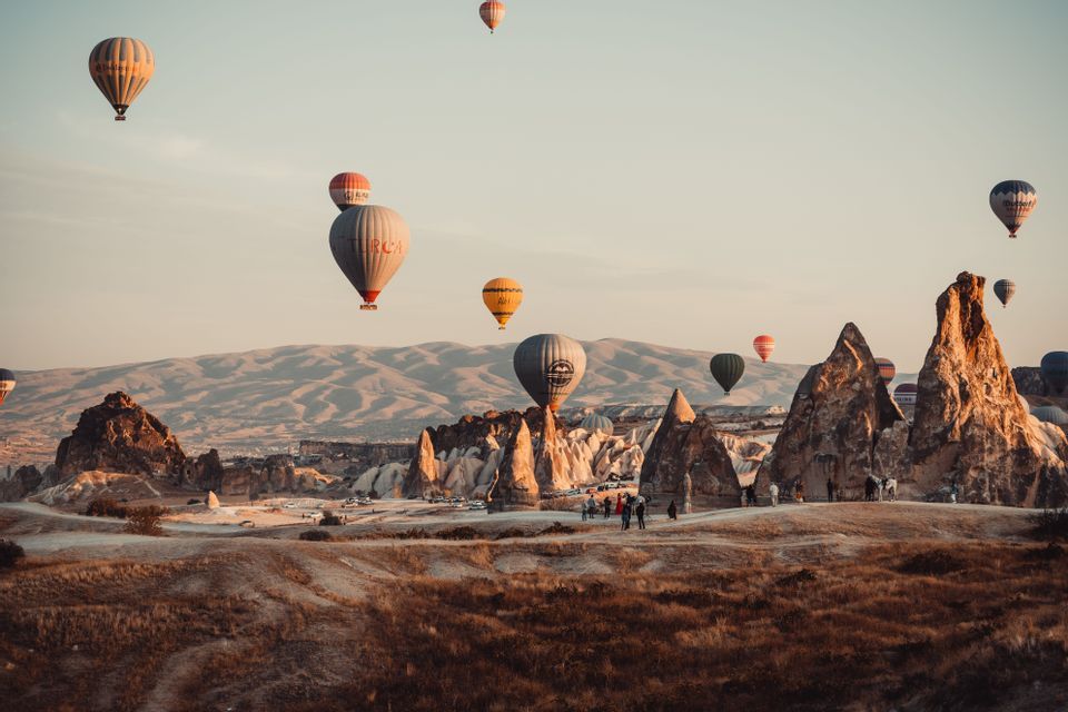 Heißluftballons schweben über einer Landschaft aus einzigartigen Felsformationen, während eine Gruppe von Menschen vom Boden aus zuschaut.
