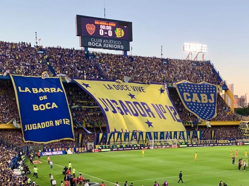 Uno stadio del Boca Juniors gremito con tifosi che espongono grandi striscioni blu e gialli prima di una partita di calcio.