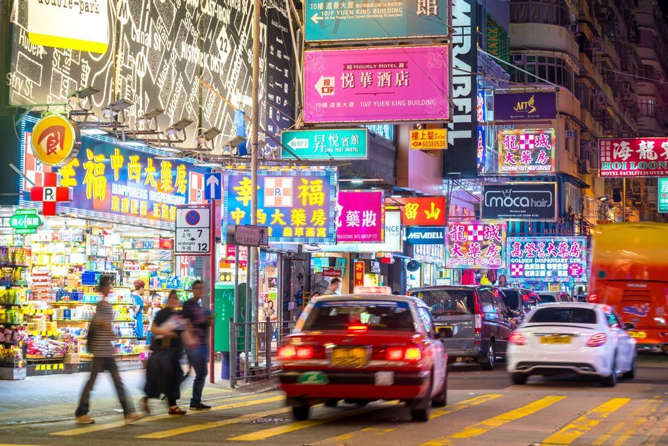 A busy city street at night with motion-blurred cars and pedestrians under dense, glowing neon signs with Chinese characters.