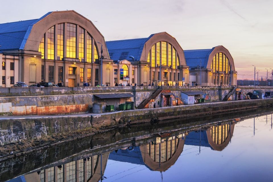 Trois grands bâtiments arqués avec des fenêtres éclairées en doré se reflétant dans un canal au coucher du soleil.