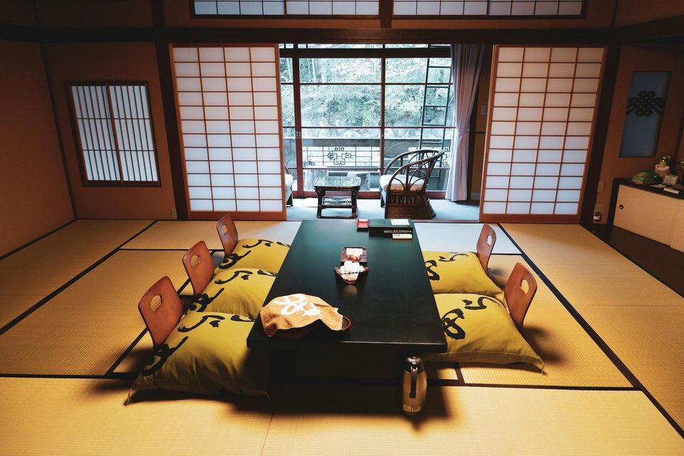 A traditional Japanese room with a low table and floor cushions on tatami mats, with shoji screens in the background.