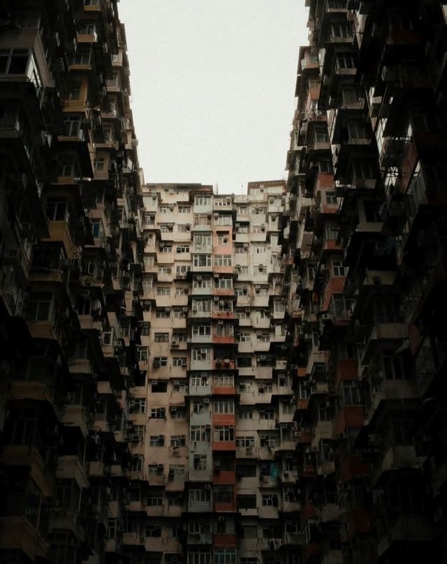 Vista dal basso verso l'alto delle facciate di edifici residenziali fittamente raggruppati sotto un cielo coperto.