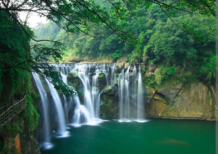 Una vasta cascata con flussi d'acqua a lunga esposizione si riversa in una piscina turchese, circondata da una foresta lussureggiante e verde.