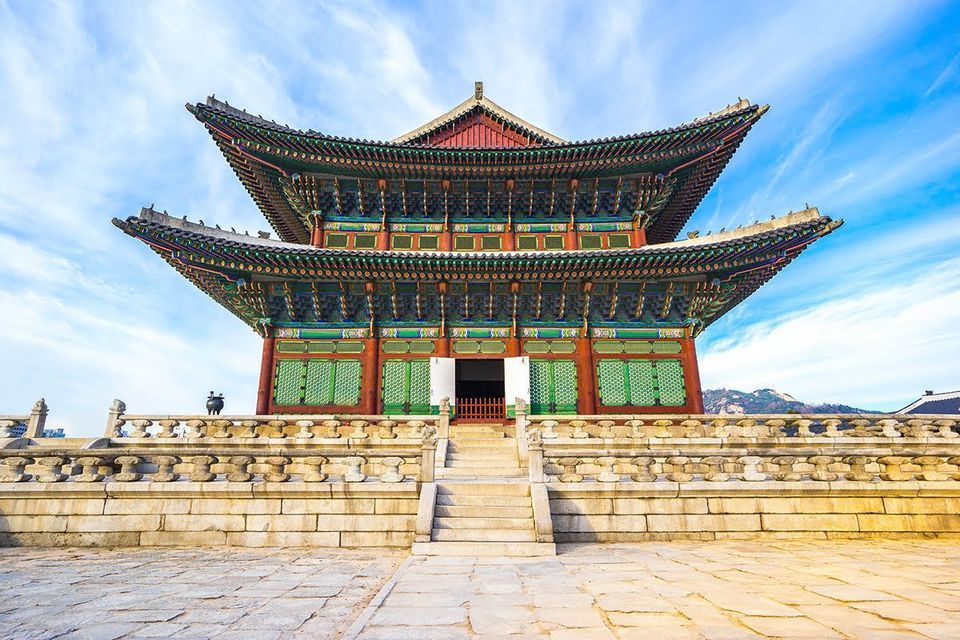 Un palazzo tradizionale dell'Asia orientale con un tetto colorato a più livelli si erge su una terrazza in pietra sotto un cielo azzurro brillante.