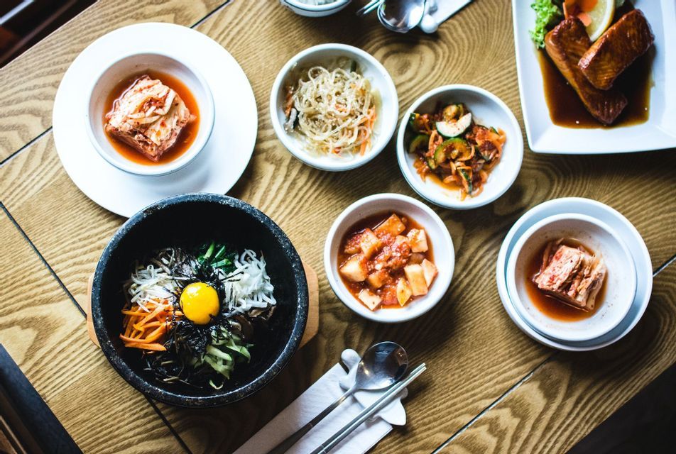 Una vista dall'alto di un pasto coreano con bibimbap in ciotola di pietra, kimchi e altri contorni disposti su un tavolo di legno.