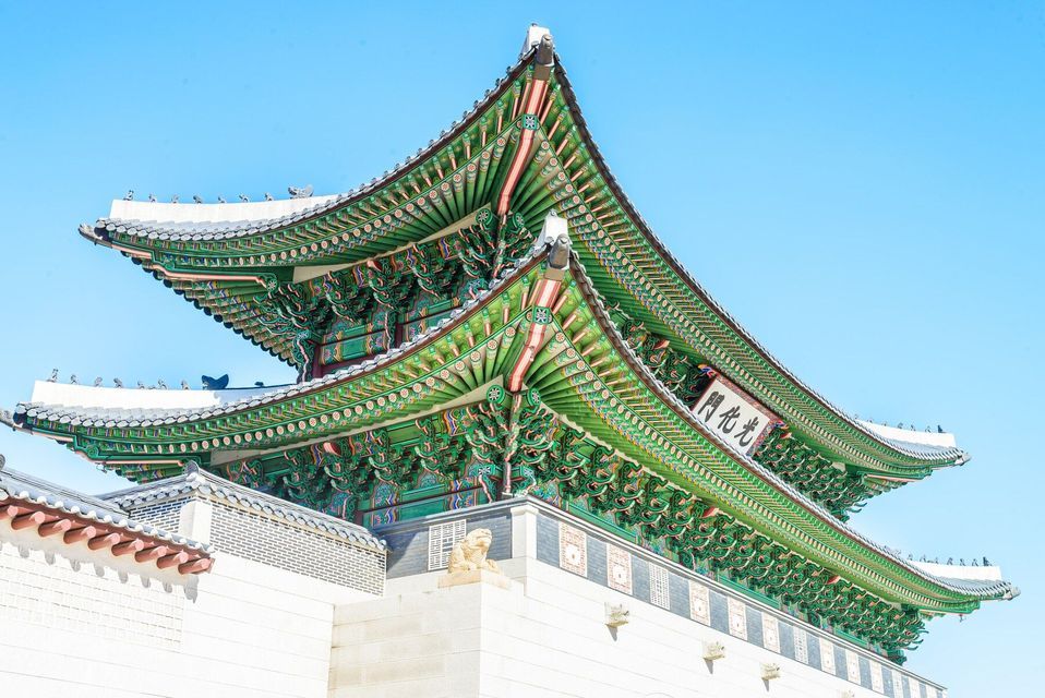 Il tetto ornato, con tegole verdi, di un tradizionale tempio asiatico poggia su un muro di pietra bianca sotto un cielo azzurro limpido.