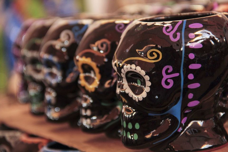 Primer plano de tazas de calavera Calavera de cerámica negra con diseños coloridos pintados a mano, alineadas.