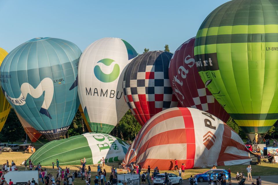 Mongolfiere colorate in varie fasi di gonfiaggio su un campo erboso durante un festival affollato.
