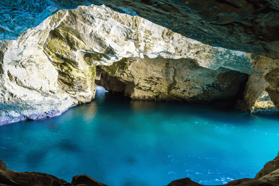 Una vista dall'interno di una grotta marina che si apre su acque turchesi, circondata da formazioni rocciose illuminate.