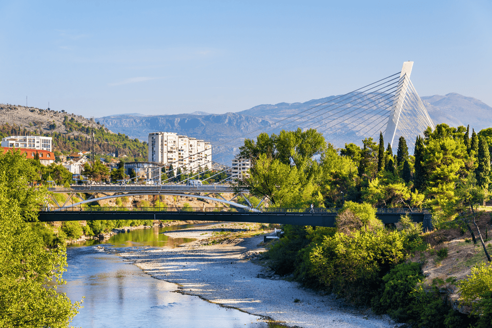 Un moderno ponte strallato e altri ponti più piccoli attraversano un fiume in una città circondata da alberi verdi e montagne distanti.