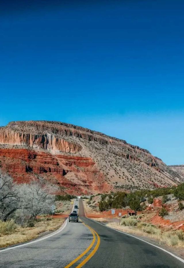 Eine kurvenreiche Straße mit Autos schlängelt sich durch eine Wüstenlandschaft zu einem geschichteten roten Felsplateau.