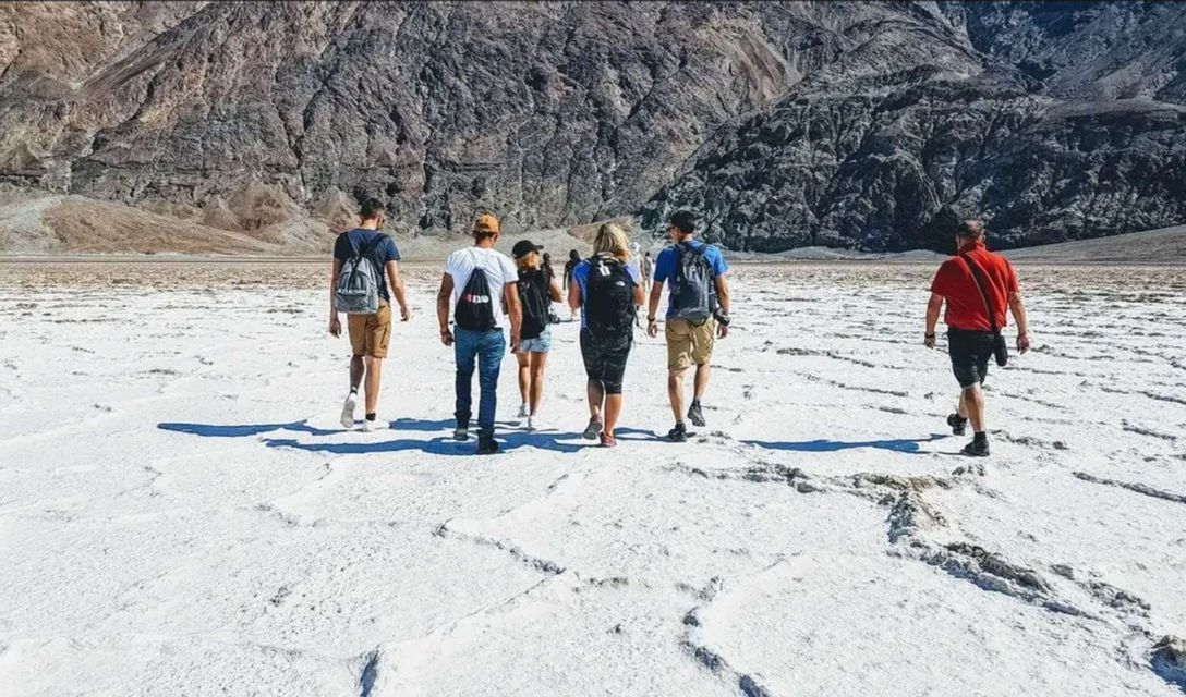 A WeRoad group trip walks across a vast, white salt flat with a rocky mountain range in the background.