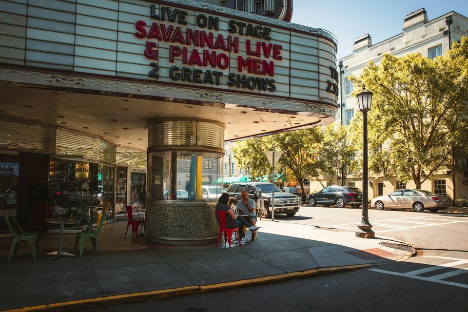 A classic theater entrance with a large marquee advertising 'Savannah Live' on a sunny street corner.
