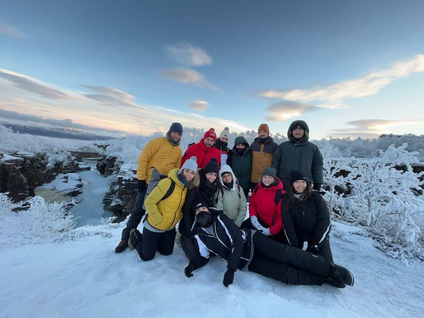 Eine WeRoad-Gruppenreise posiert für ein Foto in einer verschneiten Landschaft neben einer gefrorenen Flussschlucht bei Sonnenaufgang.