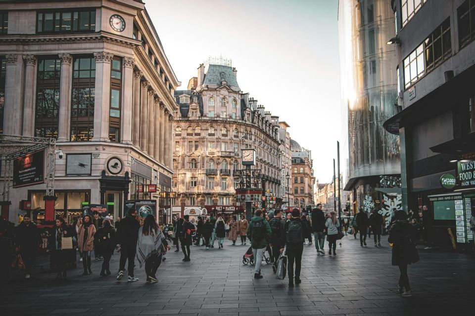 Una folla di persone passeggia lungo un'ampia via pedonale lastricata, fiancheggiata da edifici storici e moderni in città.
