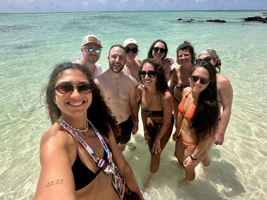 Un groupe WeRoad en voyage prend un selfie collectif dans une eau de mer claire et peu profonde sous un ciel lumineux.