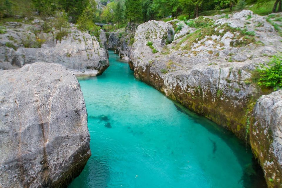 Une rivière turquoise limpide traverse une gorge étroite, bordée de grands rochers gris et d'arbres verts.