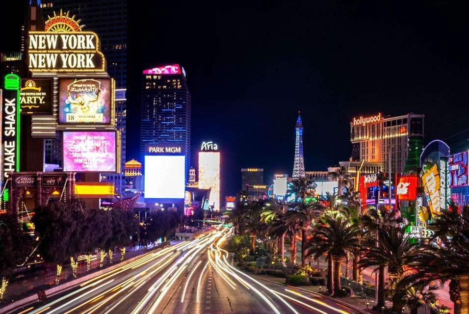 A long-exposure night shot of a busy city street with light trails from cars and bright neon signs on buildings.