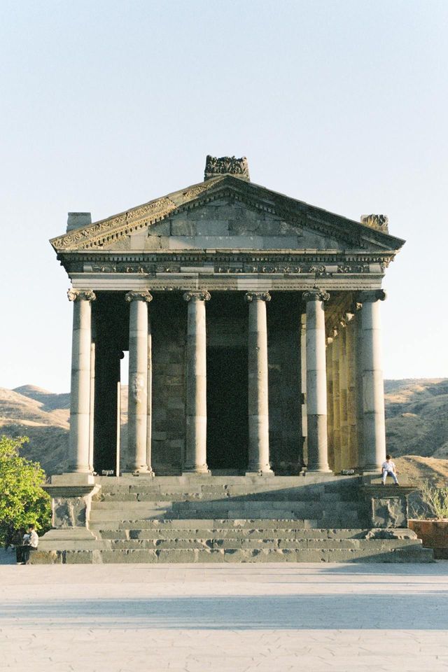 Un temple de pierre avec de grandes colonnes et des marches, dressé sur un fond de collines arides et vallonnées.