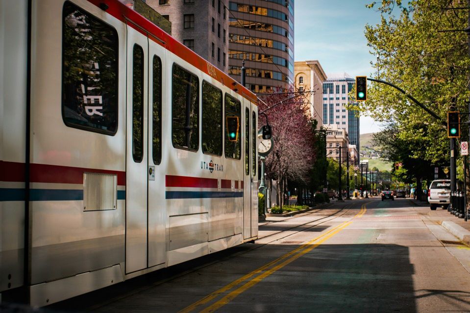 A white UTA Trax tram on a track running down a tree-lined city street next to modern buildings.