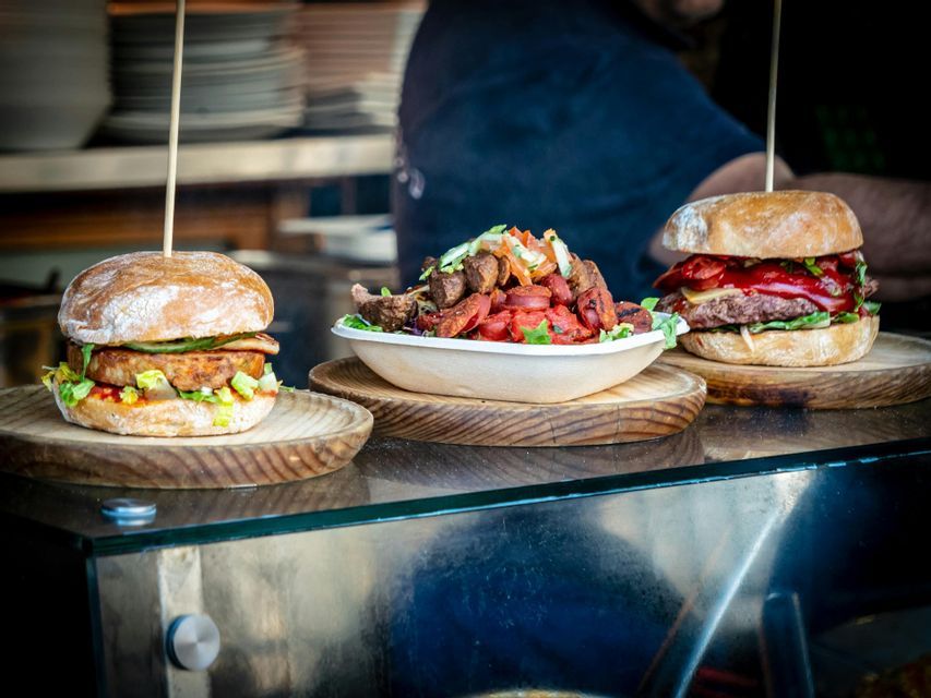 Two burgers and a salad bowl with meat and vegetables are displayed on a stainless steel counter at a food stall.