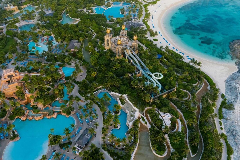 An aerial view of a large tropical resort with pools, water slides, and palm trees next to a white sand beach.