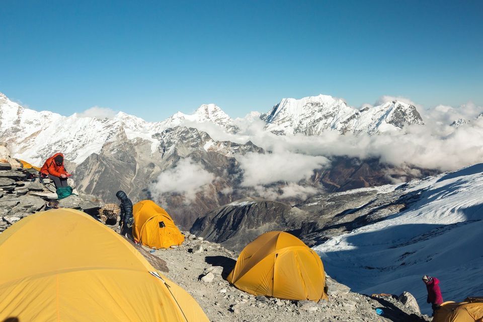 Un groupe WeRoad campe dans des tentes jaune vif sur un flanc de montagne rocheux, avec une vaste chaîne de sommets enneigés en arrière-plan.