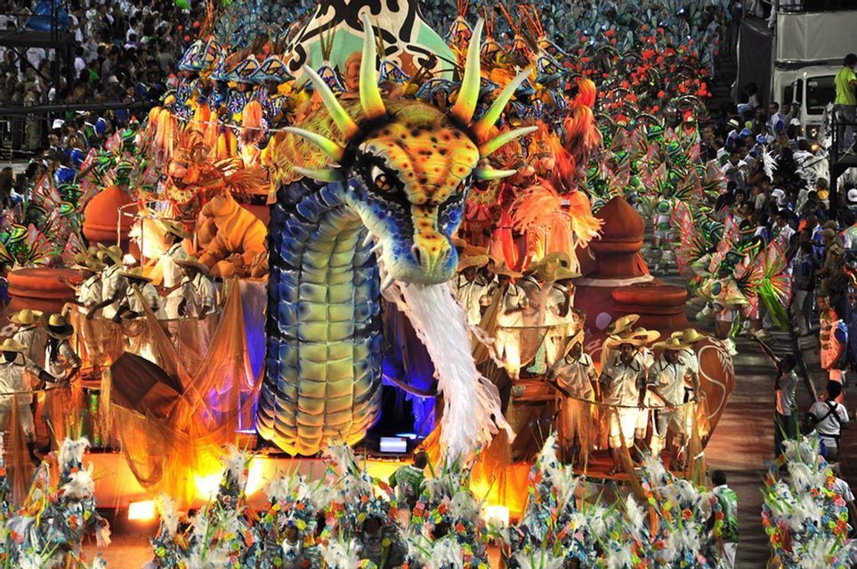 Ein großer, farbenprächtiger Drachenwagen bewegt sich während eines Karnevals durch eine Parade, umgeben von Darstellern in lebhaften Kostümen.