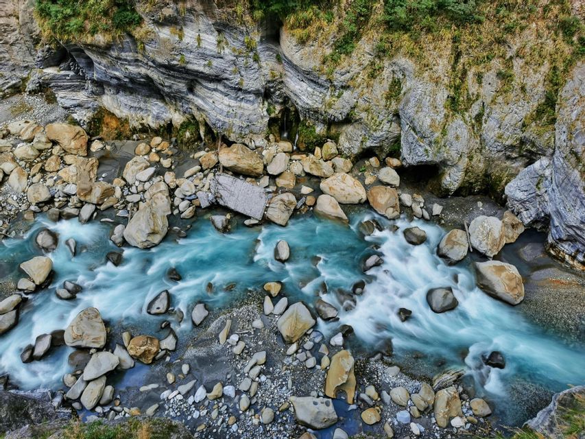Vue aérienne en pose longue d'une rivière turquoise coulant impétueusement à travers des gorges rocheuses parsemées de gros rochers.