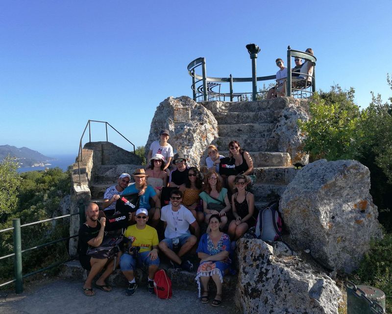 Eine WeRoad-Gruppe posiert für ein Foto auf Steinstufen an einem Aussichtspunkt mit Blick auf Meer und Küste.