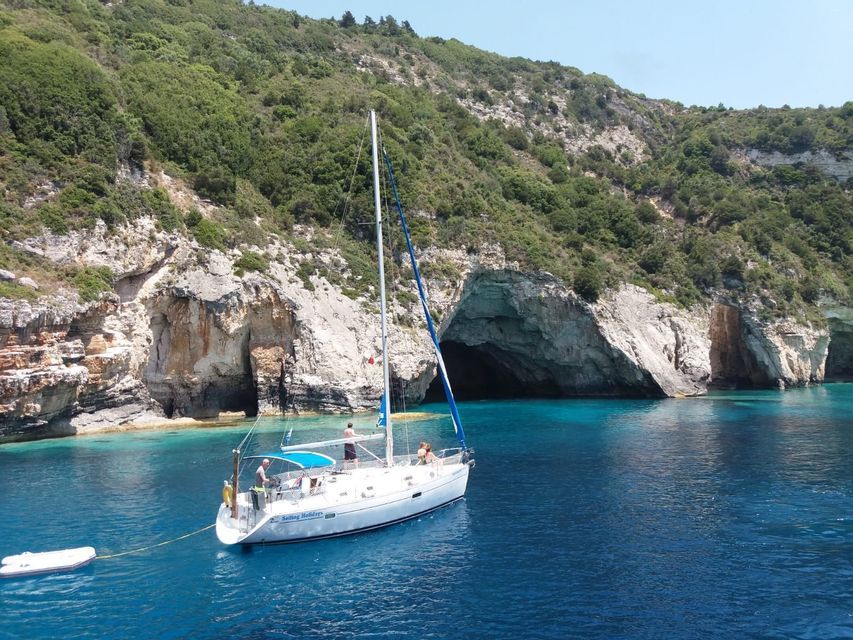 Eine WeRoad Gruppenreise auf einem Segelboot gleitet über ruhiges, türkisfarbenes Wasser in einer Bucht mit Meereshöhlen und einer Klippe.