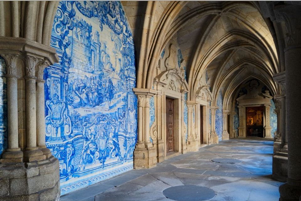 An empty stone hallway with Gothic arches and one wall entirely covered in a blue and white azulejo tile mural.