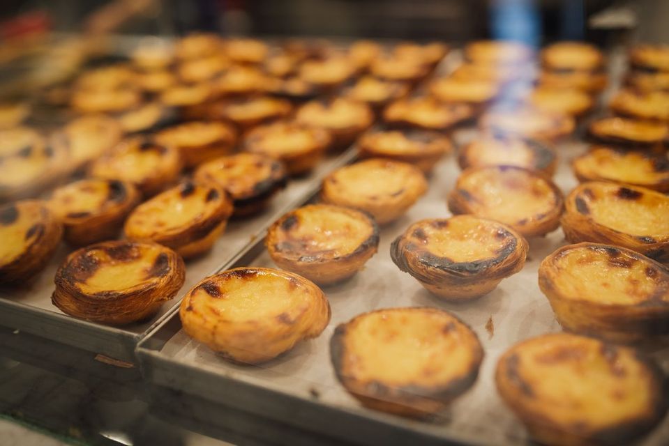 A close-up of freshly baked Portuguese egg tarts, Pastéis de Nata, with caramelized tops arranged on metal baking trays.