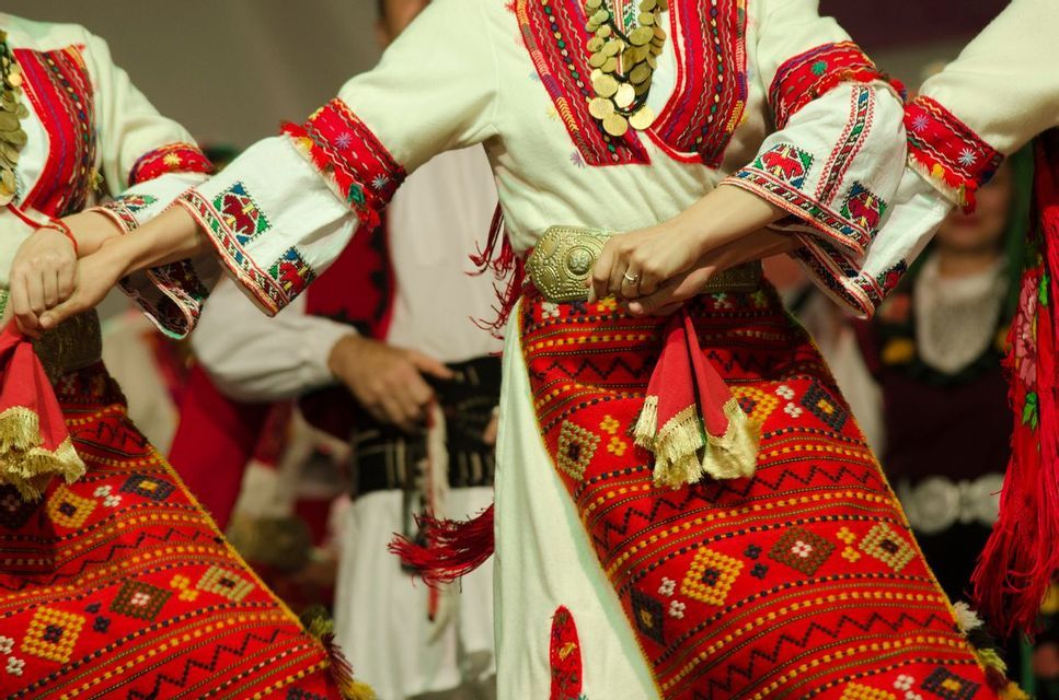 A close-up of people in traditional embroidered folk costumes holding hands while performing a folk dance.