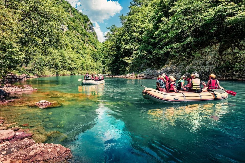 A WeRoad group trip rafting in two inflatable boats on a turquoise river that winds through a lush green canyon.