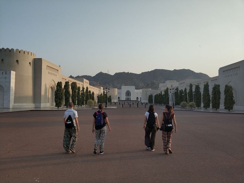 A WeRoad group trip of four people walking from behind across a large plaza towards a grand building with mountains in the background.