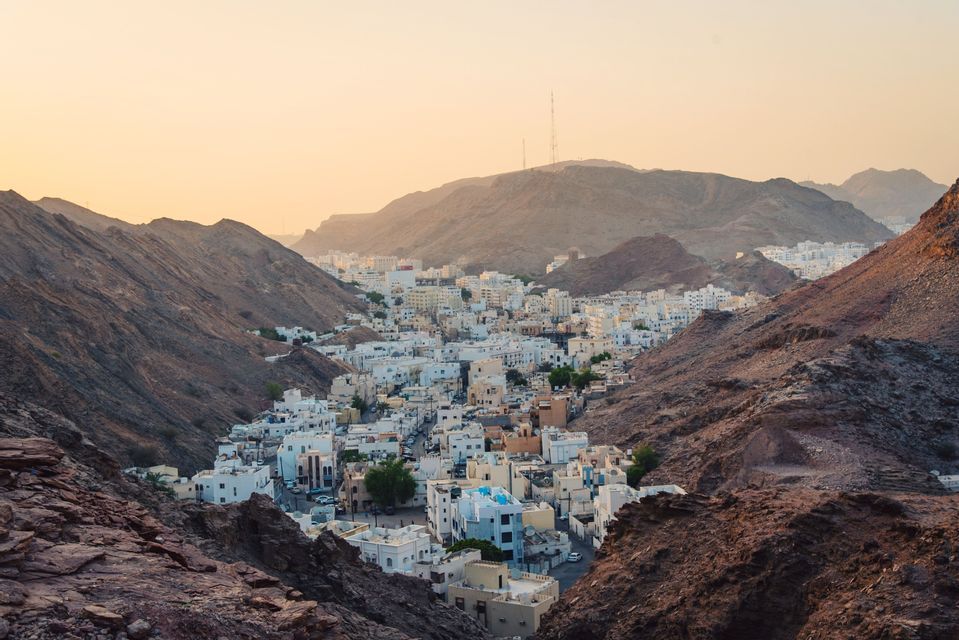 Una ciudad de edificios blancos anidada en un valle entre montañas escarpadas y rocosas durante un atardecer brumoso.