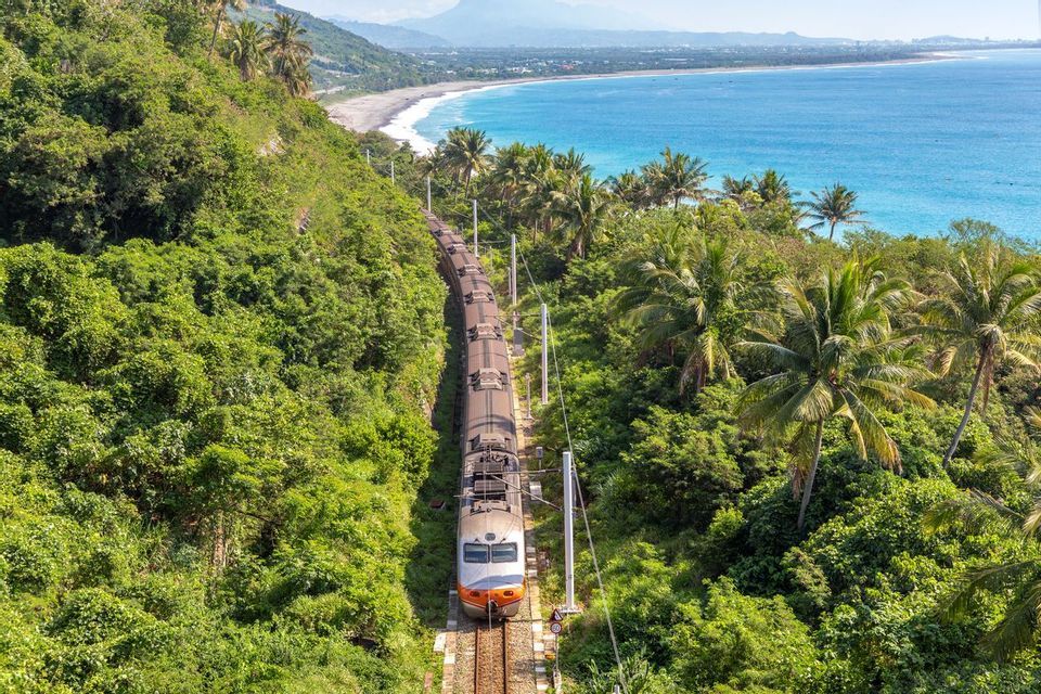 Vue aérienne d'un train traversant une forêt luxuriante le long d'une côte tropicale.