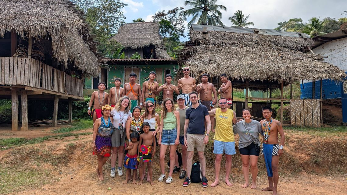 Des voyageurs de WeRoad posent pour une photo avec des membres d'une communauté indigène devant des cabanes traditionnelles au toit de chaume.