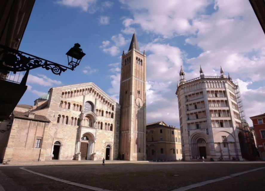 Una cattedrale storica, un campanile e un battistero si ergono in un'ampia piazza pubblica sotto un cielo parzialmente nuvoloso.